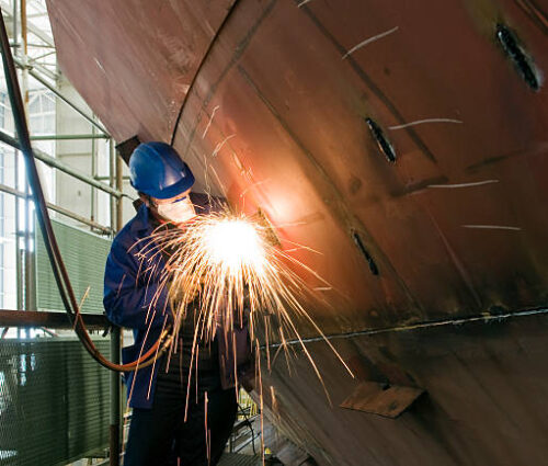 Welding new steel plates on a ship's hull during repair work on a ship in a dry dock.